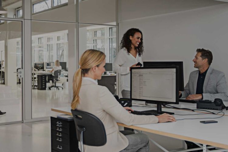 two women and one man in a white office environment with a desktop PC