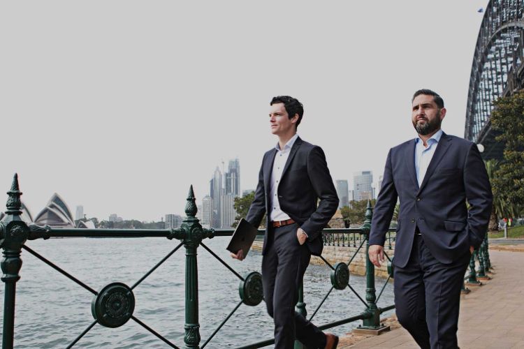 two men in suits walking along Sydney Harbour